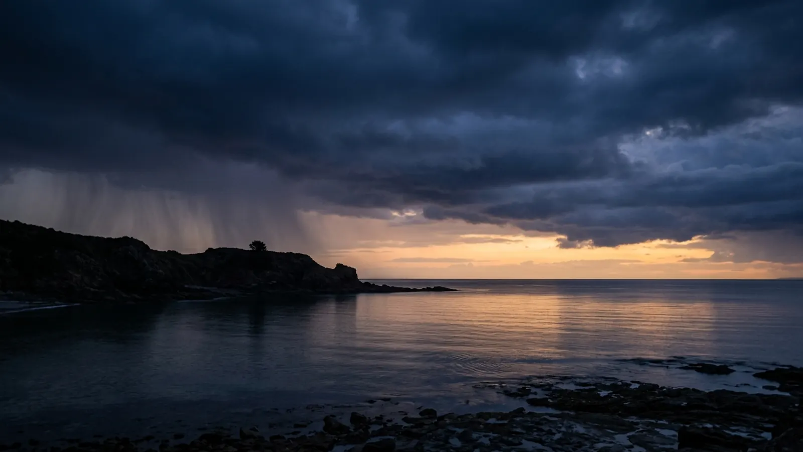 Storm clouds clearing over a quiet bay as dawn breaks on the horizon
